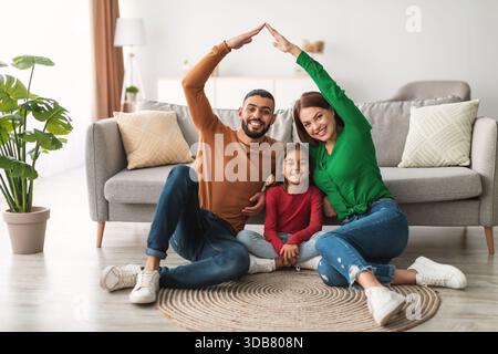 Glückliche Familie, die zu Hause eine Hütte der Hände über ihre lächelnde Tochter erschafft Stockfoto