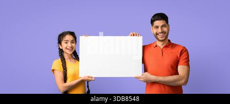 Zwei Freunde halten ein leeres Schild vor einem farbenfrohen Hintergrund in einer fröhlichen Umgebung Stockfoto