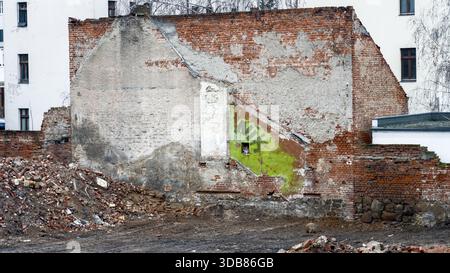 Eine verfallene Ziegelmauer mit Graffiti steht auf einer Abbruchstelle, umgeben von Schutt in einer städtischen Umgebung. Stockfoto