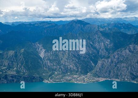 Blick aus der Vogelperspektive auf Limone sul Garda am Gardasee, umgeben von steilen Kalksteinklippen und bewaldeten Gipfeln unter Sommerwolken. Stockfoto