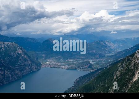 Hohe Aussicht vom Mount Baldo über den nördlichen Gardasee mit steilen Kalksteinhängen, Malcesine Küste und stürmischen Sommerwolken. Stockfoto