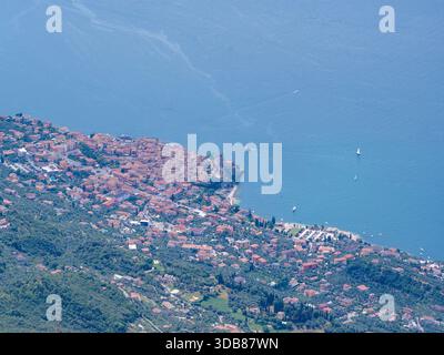 Blick aus der Vogelperspektive auf Malcesine am Gardasee mit Blick auf das mittelalterliche Scaliger-Schloss, Terrakottadächer, Hafenmauern aus Stein und Boote auf blauem Wasser. Stockfoto