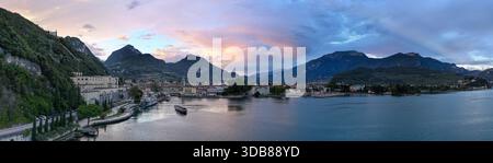 Panoramablick bei Dämmerung über den Hafen von Riva del Garda am Gardasee, umgeben von steilen alpinen Hängen und historischen Gebäuden am Wasser. Stockfoto