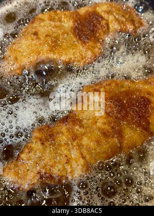 Zwei goldbraune panierte Stücke werden in heißem, sprudelndem Öl gebraten. Die Textur ist rau und strukturiert, mit einigen dunkleren braunen Flecken. Stockfoto