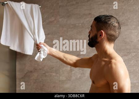 Muskulöser junger arabischer Mann, der sich nach der Dusche in einem modernen Badezimmer zu Hause abtrocknet Stockfoto