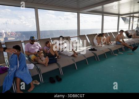 Kreuzfahrtpassagiere entspannen sich in Liegestühlen auf dem offenen Deck und genießen Sonne, Getränke und Meeresluft während eines Tages auf dem Meer. Stockfoto