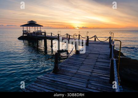 Erleben Sie einen ruhigen Sonnenuntergang über den ruhigen Gewässern von Koh Kood Island, Thailand. Der hölzerne Pier erstreckt sich bis ins Meer, perfekt für abendliche Spaziergänge und Entspannung in der Natur. Stockfoto