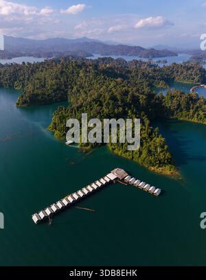 Erkunden Sie die atemberaubende Schönheit des Cheow Lan Lake in Khao Sok, Thailand, wo das smaragdgrüne Wasser auf grüne Inseln trifft. Ein ruhiger Pier erstreckt sich bis in den See und lädt Besucher ein, die Pracht der Natur zu genießen. Stockfoto