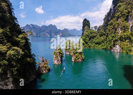 Helles Sonnenlicht beleuchtet den atemberaubenden Cheow Lan Lake in Khao Sok, Thailand. Üppige grüne Landschaften umgeben das ruhige Wasser, während Kajakfahrer durch die ruhige Umgebung gleiten. Stockfoto