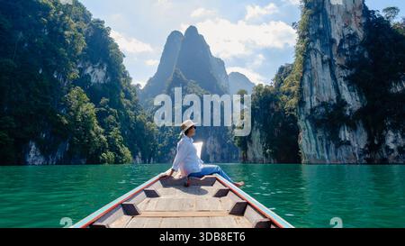 Ein Reisender sitzt ruhig auf einem Boot am Cheow Lan Lake in Khao Sok, Thailand, umgeben von atemberaubenden Kalksteinklippen und üppigem Grün. Das klare, türkisfarbene Wasser reflektiert den hellblauen Himmel. Stockfoto