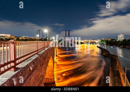 Long exposure captures Stone Arch Bridge over Mississippi River in Minneapolis, USA. Illuminated arches reflect in flowing water under a night sky Stockfoto