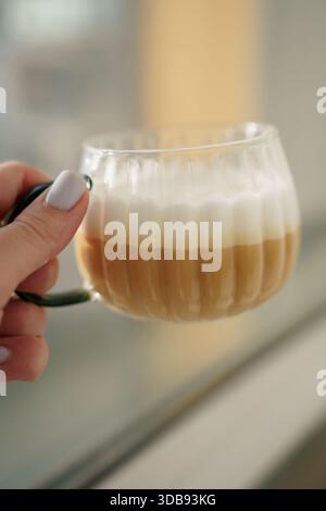 Nahaufnahme einer Hand, die eine gerippte Glasschale mit Lagenlatte vor einem sanft verschwommenen Hintergrund in warmen, weichen Tönen hält, die ein gemütliches und gemütliches Ambiente schaffen Stockfoto