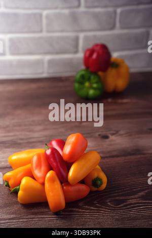 Eine lebhafte Auswahl kleiner roter, gelber und oranger Paprika auf einer strukturierten Holzoberfläche mit einem verschwommenen Hintergrund mit drei größeren Be Stockfoto