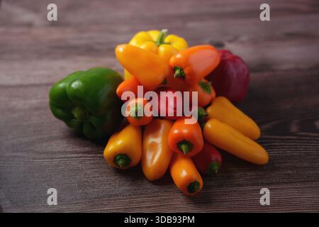 Lebhafte Mischung aus Paprika auf rustikaler Holzoberfläche mit satten Farben und strukturiertem Hintergrund, die Frische und kulinarische Vielfalt hervorheben Stockfoto
