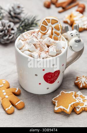 Rentierbecher gefüllt mit heißer Schokolade, Marshmallows und Lebkuchenbonbons mit festlicher Einrichtung Stockfoto