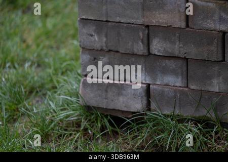 Stapel rechteckiger Pflastersteine ordentlich auf einer Holzpalette im Freien auf Gras angeordnet. Das Bild zeigt Baumaterialien, die für die Landschaftsgestaltung vorbereitet sind Stockfoto
