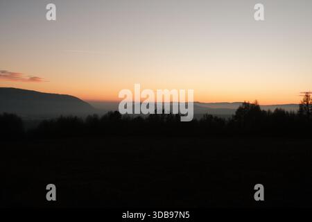 Ruhige Bergsicht bei Sonnenuntergang, Silhouetten von Bäumen schaffen eine beruhigende, dramatische Szene. Stockfoto