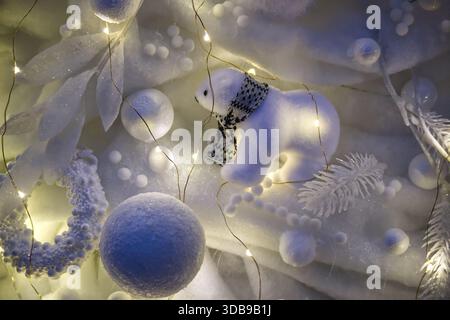Eine flauschige Eisbärenfigur mit Schal ist umgeben von schneebedeckten Ornamenten und funkelnden Lichtern, die eine bezaubernde Winterszene schaffen Stockfoto