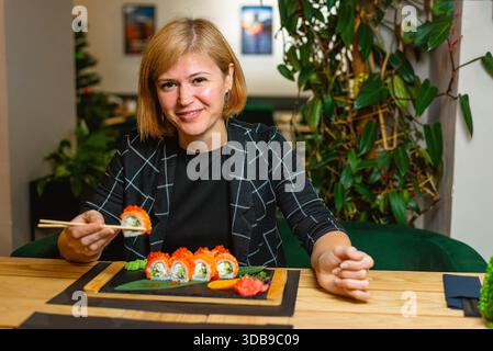 Lächelnde Frau bereitet sich darauf vor, einen ordentlich angeordneten Teller Sushi-Brötchen zu probieren. Stockfoto
