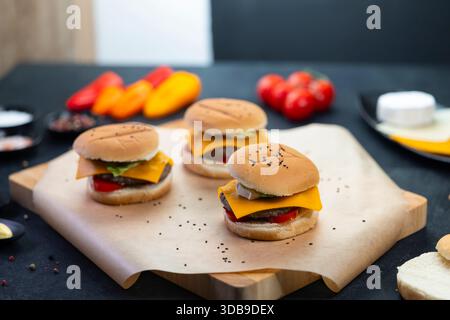 Klassische Cheeseburger-Slider mit frischen Belägen auf einem Holzbrett zum Servieren Stockfoto