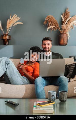 Fröhliche Paare teilen sich Momente zusammen, während sie ihr Smartphone und ihren Laptop nutzen, um die Essenz moderner Gesellschaft und Technologie in ihrem festzuhalten Stockfoto