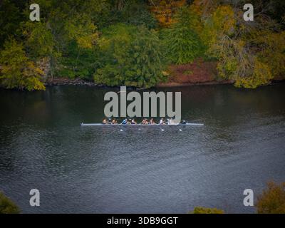 Aus der Vogelperspektive eines Ruderteams, das durch das dunkle Wasser des Charles River schneidet, eingerahmt von den herbstlichen Farbtönen der Bäume von Boston, Massachusetts, Unite Stockfoto