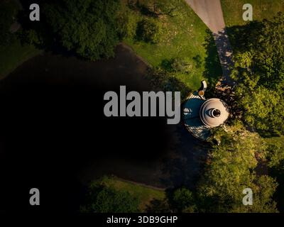 Blick aus der Vogelperspektive auf den malerischen Wasserturm am Chestnut Hill Reservoir, dessen Steinfassade das Sonnenlicht im tiefblauen Wasser und üppigem Greis reflektiert Stockfoto