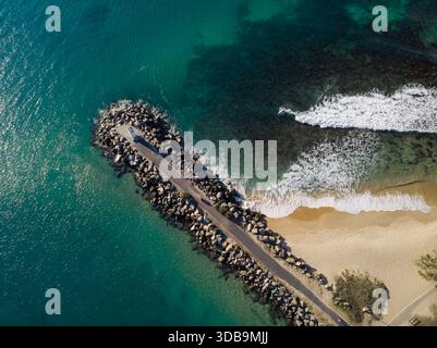 Aus der Vogelperspektive auf eine felsige Wellenbrecher, die sich in das türkisfarbene Meer ausdehnt, Wellen, die gegen die Küste krachen, Mooloolaba, Queensland, Australien. Stockfoto