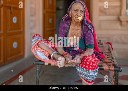 Ältere indische Bishnoi-Frau, die auf einem traditionellen Charpai vor ihrem Haus in Rajasthan, Indien, ruht. Stockfoto