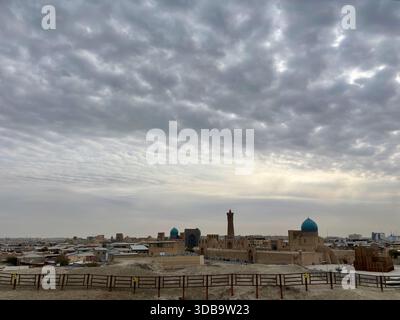 Blick auf die Skyline von Buchara mit Kalon Minaret und türkisfarbenen Kuppeln unter Wolken Stockfoto