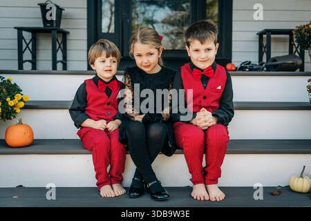 Drei formell gekleidete Kinder sitzen im Herbst auf der Veranda Stockfoto