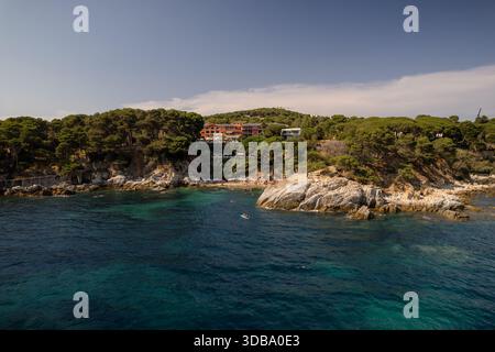 Aus der Vogelperspektive auf die zerklüftete Küste trifft auf das türkisfarbene Wasser, mit einem kleinen Strand, eingebettet unter Klippen und üppigem Grün, Platja d'Aro, Katalonien Stockfoto