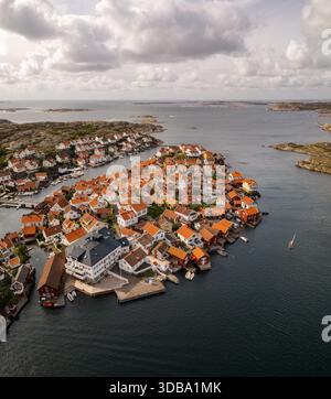 Blick aus der Vogelperspektive auf eine Ansammlung von Häusern mit rotem Dach, die sich auf einer kleinen Insel zusammenschmiegen, umgeben von dem riesigen, schimmernden Meer unter einem bewölkten Himmel, G Stockfoto