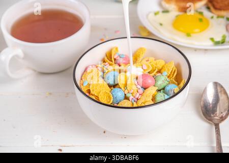 Osterfrühstück Müsli, Cornflakes mit Osterschokoladeneiern und Zuckerstreuseln, Milch oder Joghurt in Cornflakes Golden Breakfast Müsli Portion Stockfoto