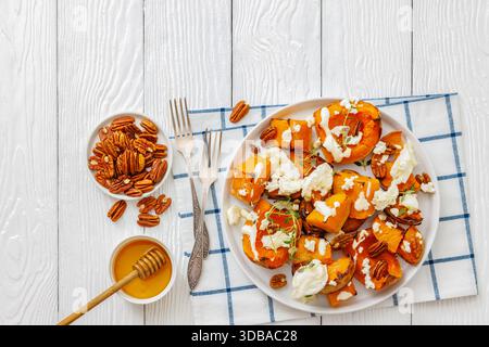 Gebackene Butternusskürbscheiben mit Mozzarella, zerbröckeltem Käse, Thymian, gerösteten Pekannüssen auf Teller auf weißem Holztisch mit Gabeln, Honig, horizontale Ansicht Stockfoto