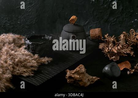 Chinesische Teezeremonie. Traditionelle handgefertigte schwarze Teekanne aus Keramik mit Holzgriff auf dunklem Teetisch. Herbststimmung. Keramik-Teetassen und getrocknetes Schilf Stockfoto