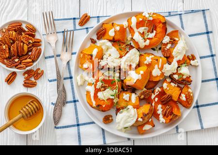 Gebackene Butternusskürbscheiben mit Mozzarella, zerbröckeltem Käse, Thymian, gerösteten Pekannüssen auf Teller auf weißem Holztisch mit Gabeln, Honig, horizontale Ansicht Stockfoto