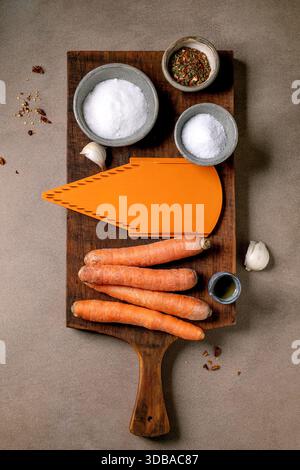 Koreanische und asiatische Küche. Zutaten für die Zubereitung von Gemüsesalat von marinierten Karotten. Rohe Karotten, Gewürze, Reibe auf hölzernem Schneidebrett. Moc Stockfoto