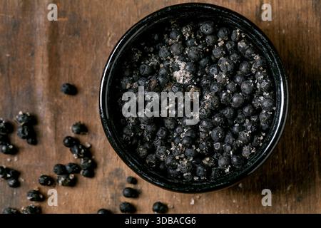 Schwarz gesalzener Fermenter Campota Pfeffer in schwarzer Keramikschale auf dunklem Holztisch. Gesunde Ernährung, scharfe Kochzutaten, asiatische Küche. Draufsicht Stockfoto
