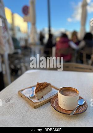 Kaffee und Kuchen auf einem Café-Tisch im historischen Ronda, Andalusien, Spanien, mit einer leicht verschwommenen Straßenszene. Stockfoto