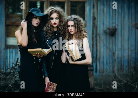 Drei alte Frauen als Hexen posieren vor einem verlassenen Gebäude mit Büchern in der Hand am Vorabend von Halloween || Model veröffentlicht Stockfoto
