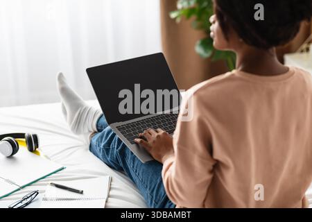 Junge Frau, die an einem Laptop in einem gemütlichen Schlafzimmer an einem entspannten Nachmittag arbeitet Stockfoto