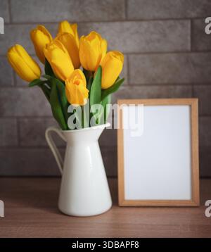 Schöne gelbe Tulpenblumen und ein leerer Bilderrahmen auf dem Tisch in der Küche Stockfoto