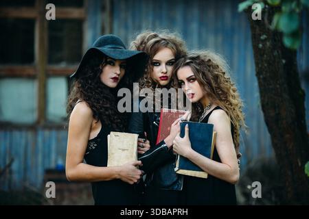 Drei alte Frauen als Hexen posieren vor einem verlassenen Gebäude mit Büchern in der Hand am Vorabend von Halloween || Model veröffentlicht Stockfoto