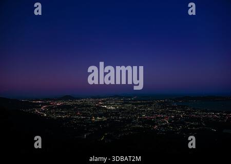 Ein atemberaubender Panoramablick bei Nacht vom Aussichtspunkt der üppigen, dunklen Hügel. Unterhalb der Küste kurvt sich die Küste anmutig, wo der Strom leuchtet. Stockfoto