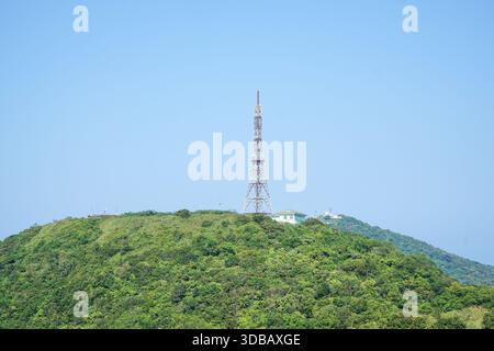 Telekommunikationsturm auf einem üppig grünen Berggipfel unter einem klaren blauen Himmel. Stockfoto