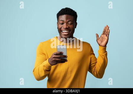 Glücklicher afroamerikanischer Kerl, der Mobiltelefon hält und gestikiert Stockfoto