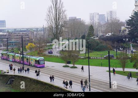 Moderne Straßenbahn, die durch ein grünes Stadtgebiet mit Fußgängern in Nantes, Frankreich, fährt und einen nachhaltigen öffentlichen Verkehr in einer europäischen Stadt zeigt. Stockfoto