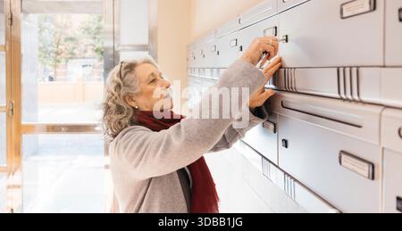 Ältere Frau, die den Schlüssel in einen gemeinschaftlichen Briefkasten einsteckte Stockfoto