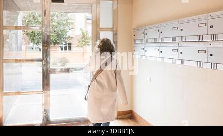 Frau verlässt das Wohngebäude mit Briefkästen in der Eingangshalle Stockfoto